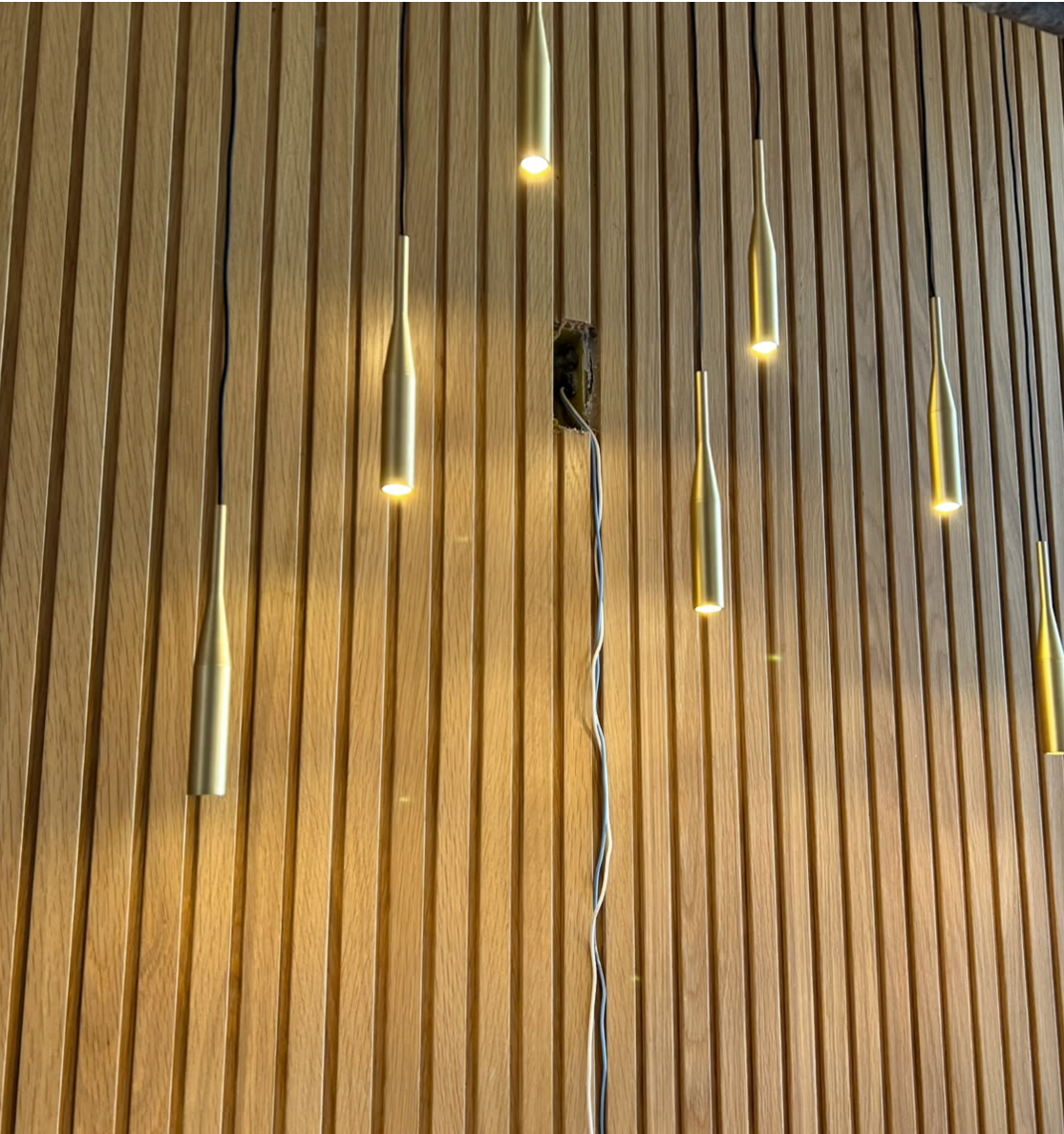 Pendentes dourados instalados sobre painel ripado de madeira