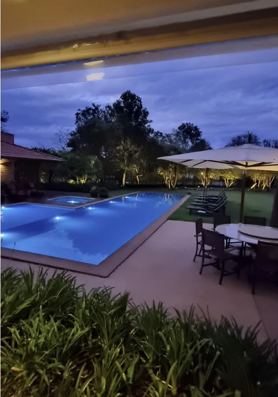 Área de lazer com piscina e paisagismo iluminados ao entardecer
