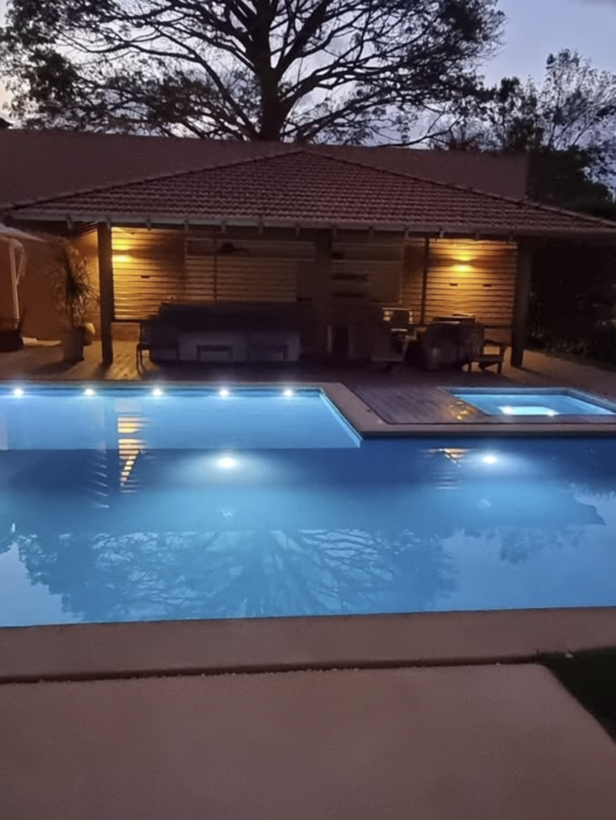 Piscina residencial iluminada com área de lazer ao fundo